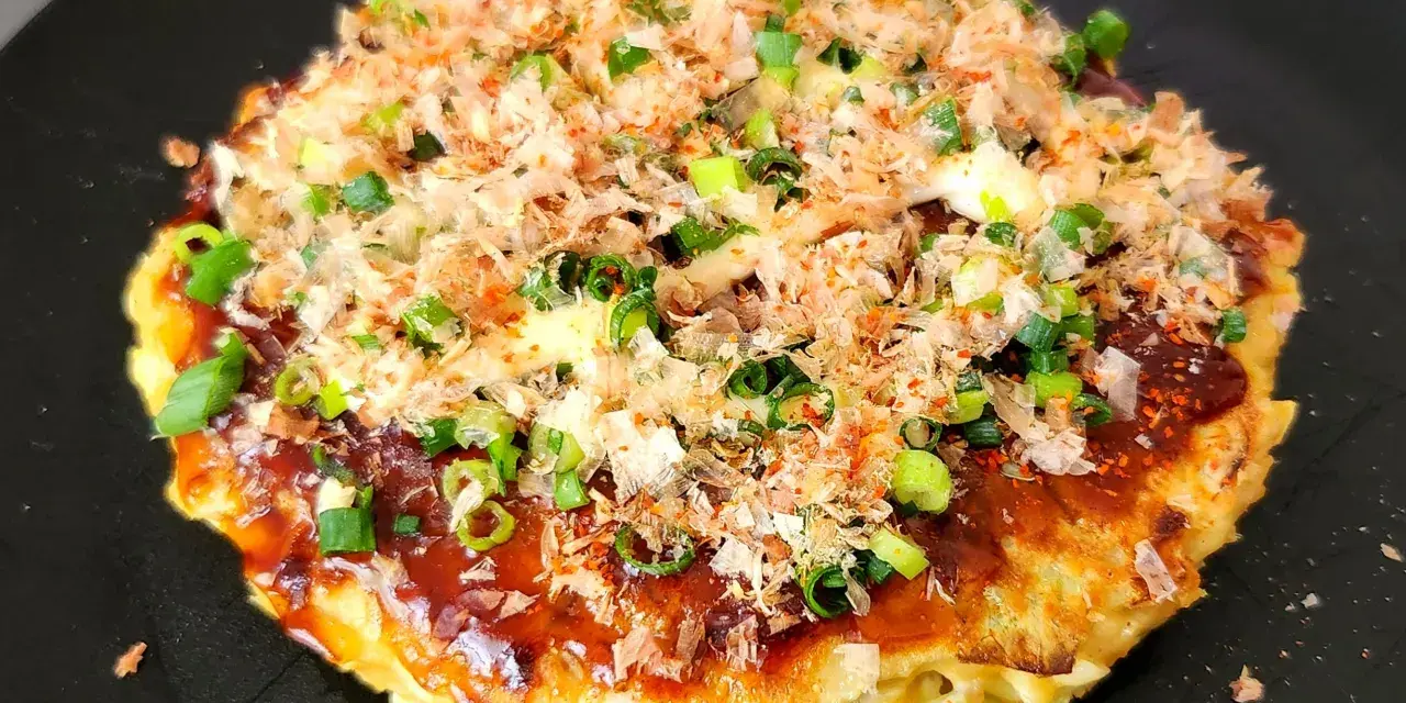 Un délicieux okonomiyaki, un plat emblématique du repas japonais maison, garni d'oignons verts et de flocons de bonite.