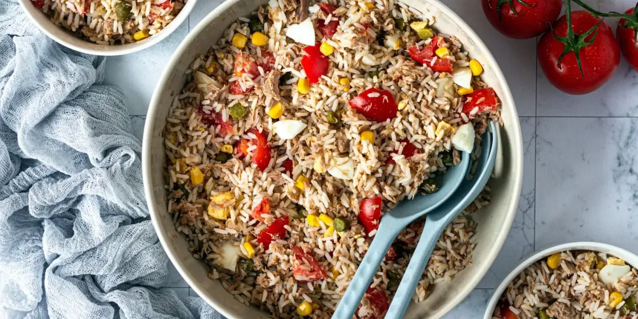 Un grand bol de salade de riz thon, garnie de tomates, maïs et œufs durs. Parfait pour un repas frais et léger.