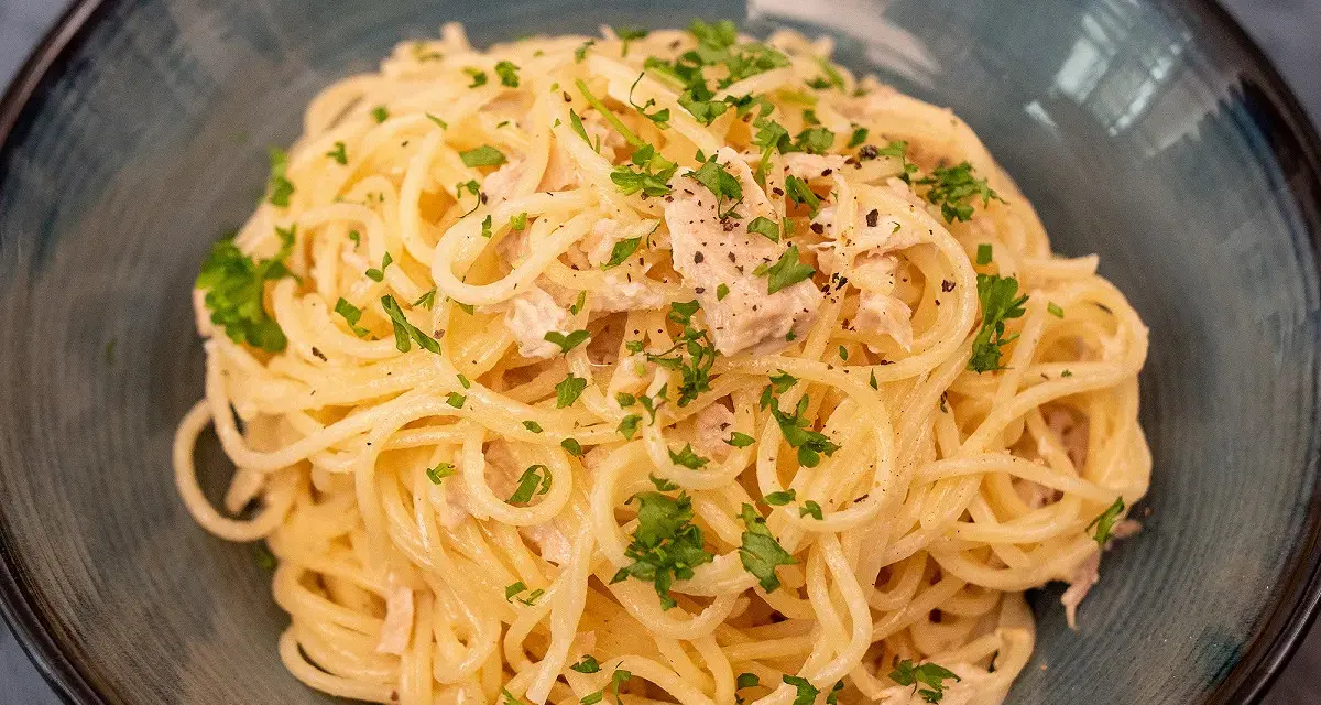 Un plat de pâtes au thon, garni de persil frais et de poivre noir, servi dans un bol bleu.