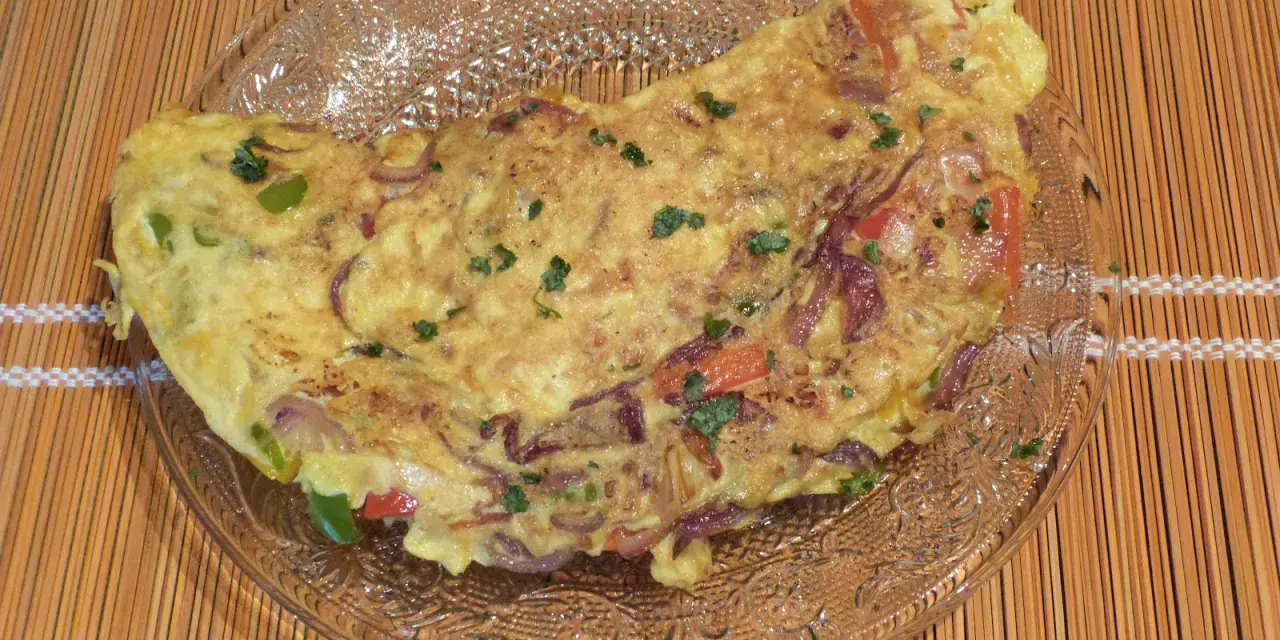 Une savoureuse omelette mexicaine garnie d'oignons rouges, de poivrons et d'herbes fraîches, servie sur une assiette en verre.
