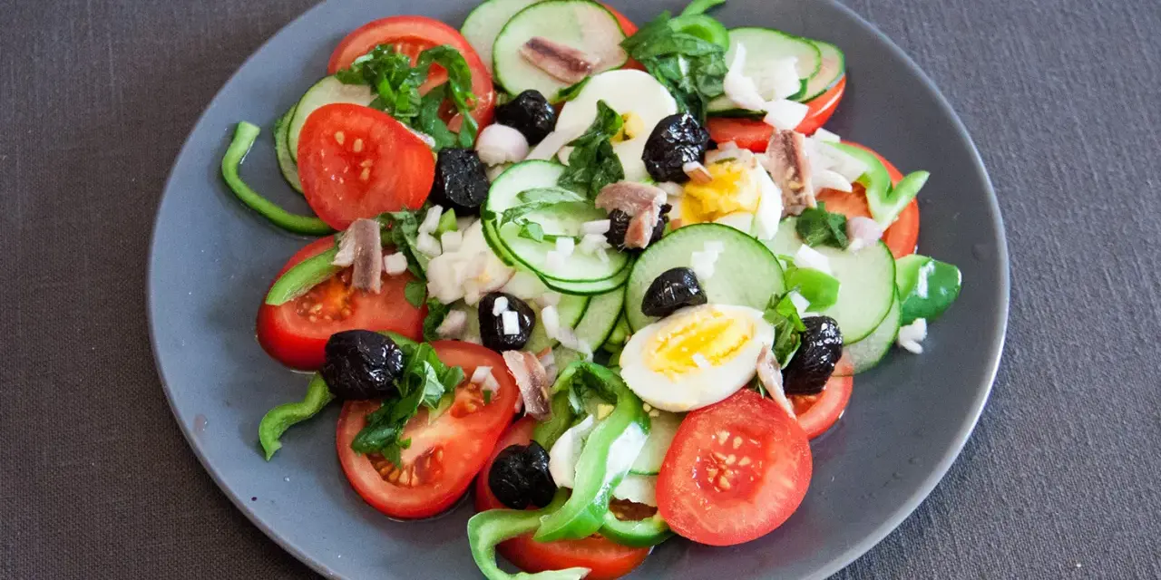 Salade niçoise colorée avec tomates, concombres, œufs, olives noires et anchois.