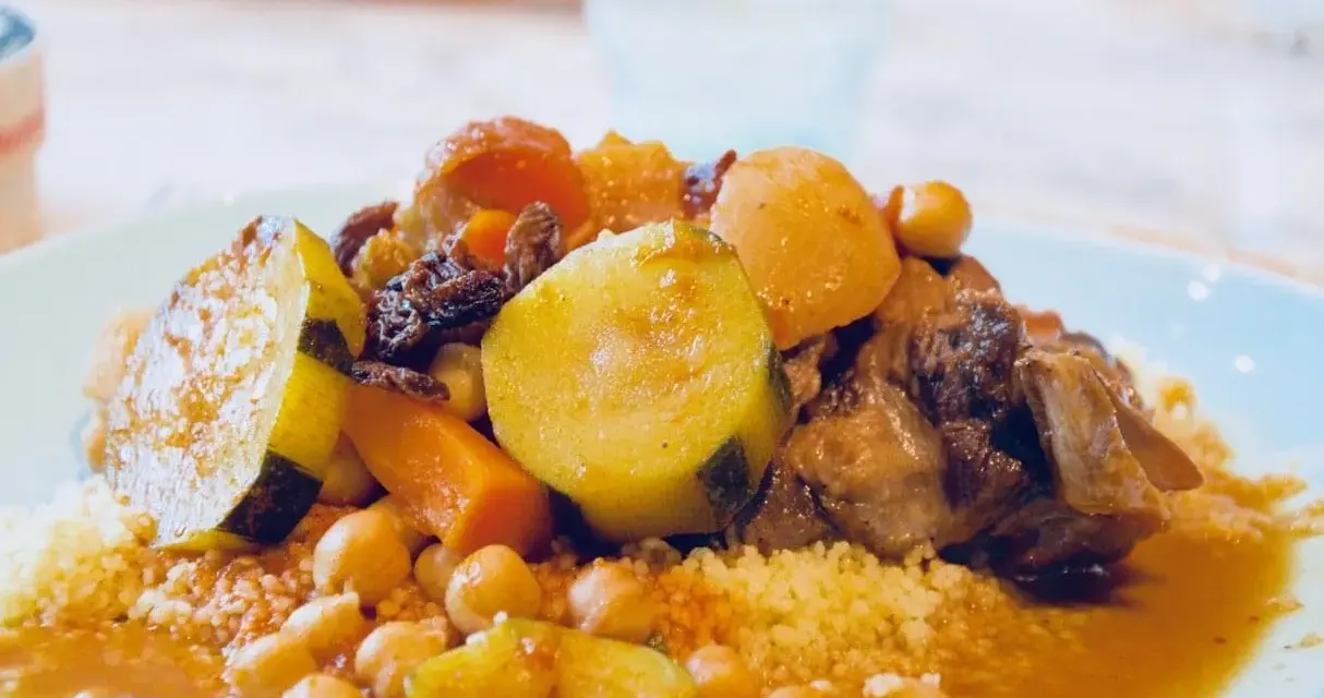 Un plat généreux de couscous algérien avec légumes, pois chiches, raisins secs et viande mijotée dans une sauce savoureuse.