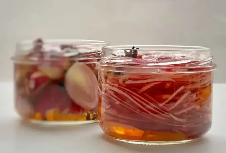 Deux bocaux de pickles d'oignon rouge, l'un avec des oignons entiers, l'autre avec des lamelles fines, baignant dans une marinade ambrée.