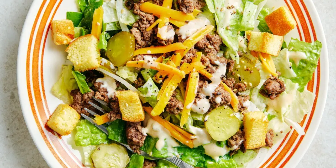 Salade Big Mac avec laitue, bœuf haché, fromage râpé, croûtons et cornichons, arrosée d'une sauce crémeuse.