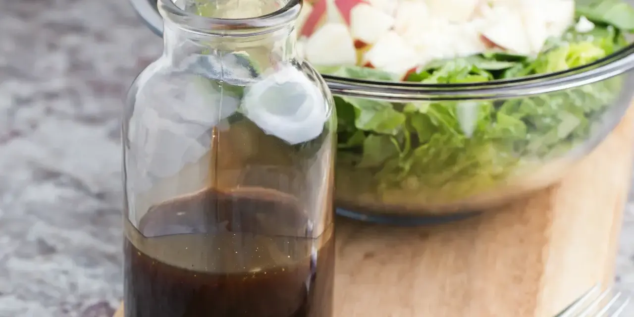 Bouteille de sauce salade facile, prête à être versée sur une salade fraîche et croquante dans un bol en verre.