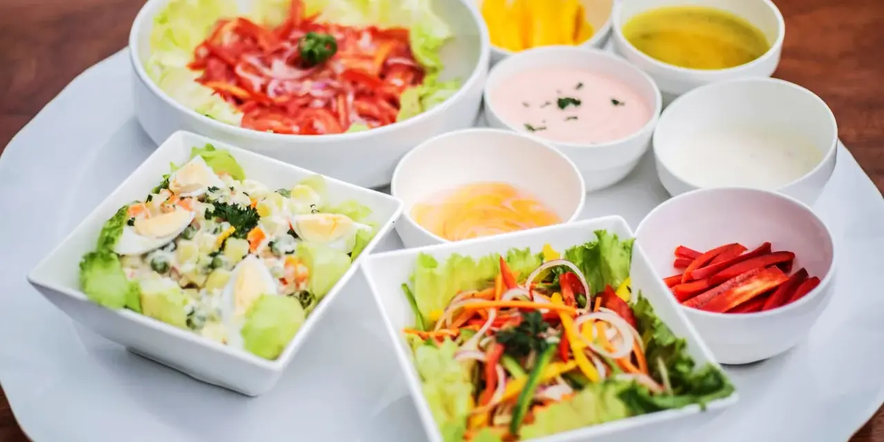 Assortiment de salades colorées avec plusieurs options de sauce pour salade, dont une rose et une verte.