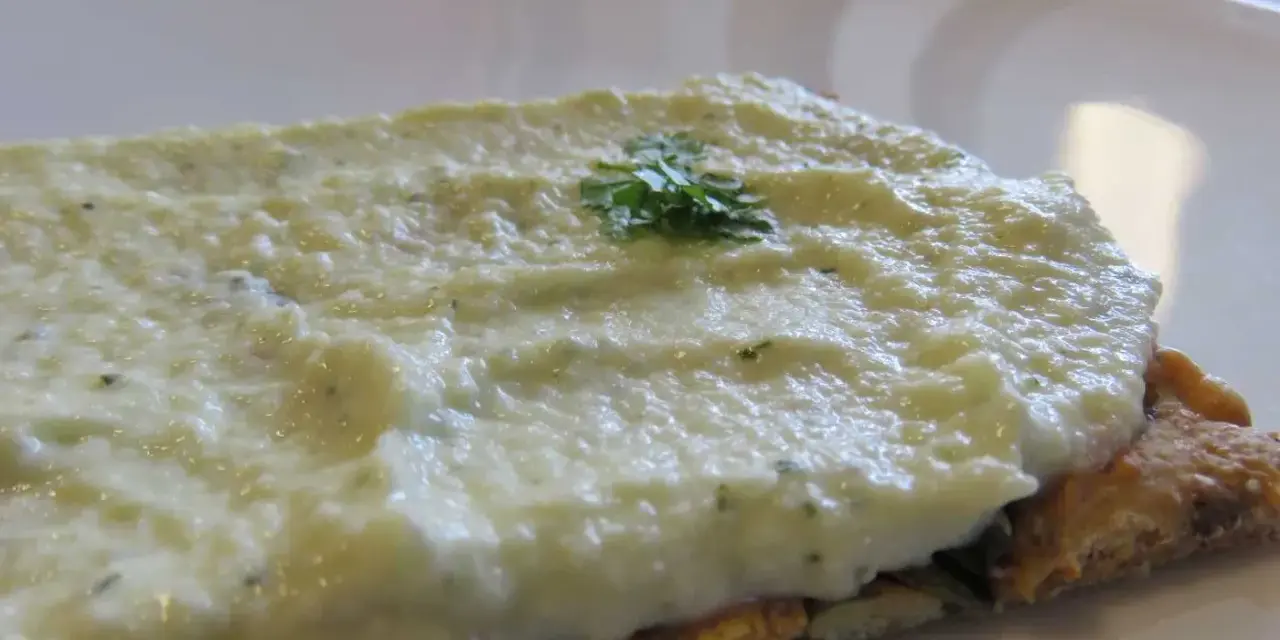 Houmous de courgette crémeux sur une tranche de pain complet, garni d'une touche de persil frais.