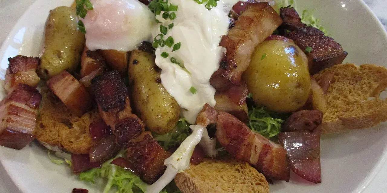 Une généreuse salade vosgienne avec des pommes de terre, lardons, œuf poché et croûtons sur un lit de verdure.