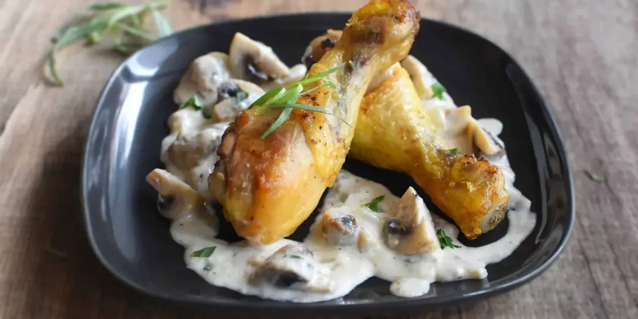 Deux pilons de poulet dorés baignent dans une sauce crémeuse aux champignons, garnie d'herbes fraîches. Un délice de poulet à la crème.