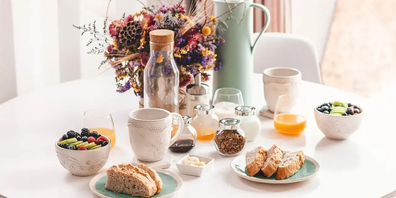 Un délicieux déjeuner vegan avec fruits frais, pain artisanal, granola et jus d'orange, présenté sur une table blanche.