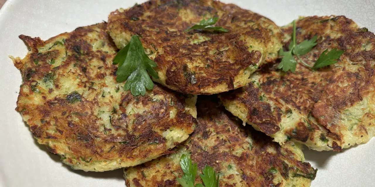 Galettes dorées de courgette et pomme de terre, garnies de persil frais, prêtes à être dégustées.