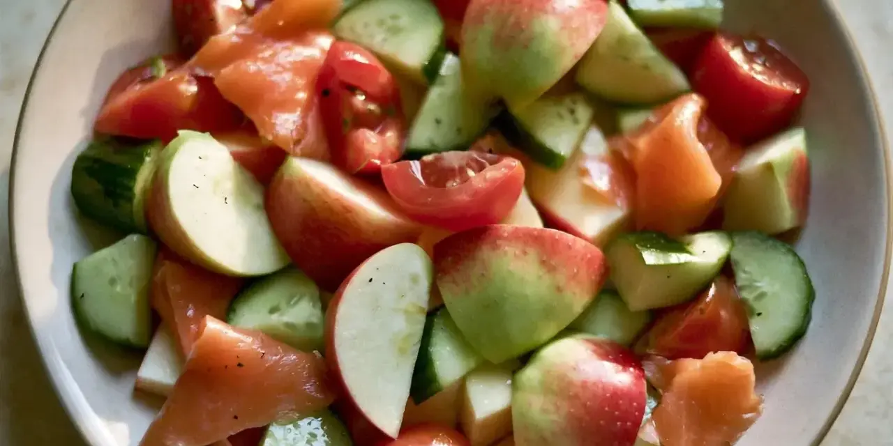 Salade fraîche et colorée : morceaux de concombre, tomates cerises, pommes rouges et saumon fumé, le tout servi dans un bol.