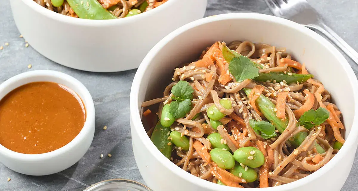 Pâtes soba aux edamames, carottes râpées et coriandre, servies avec une sauce crémeuse. Un délice sain et coloré.
