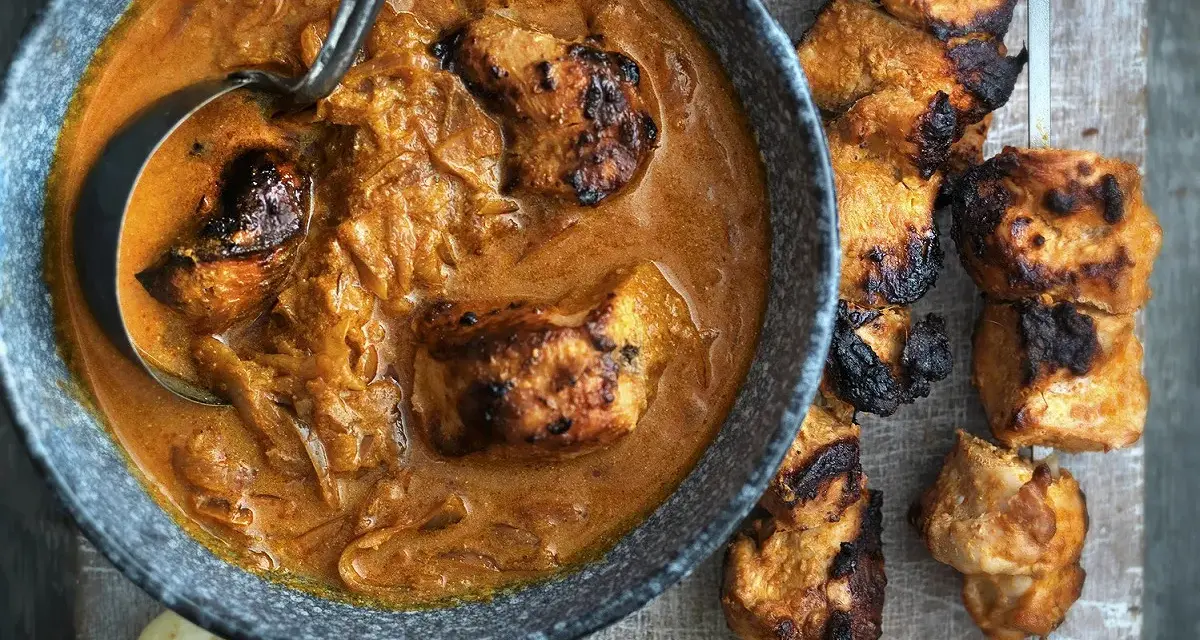 Un plat de poulet tikka savoureux, avec des morceaux de poulet grillés dans une sauce crémeuse et des accompagnements comme du pain naan et des quartiers de citron.