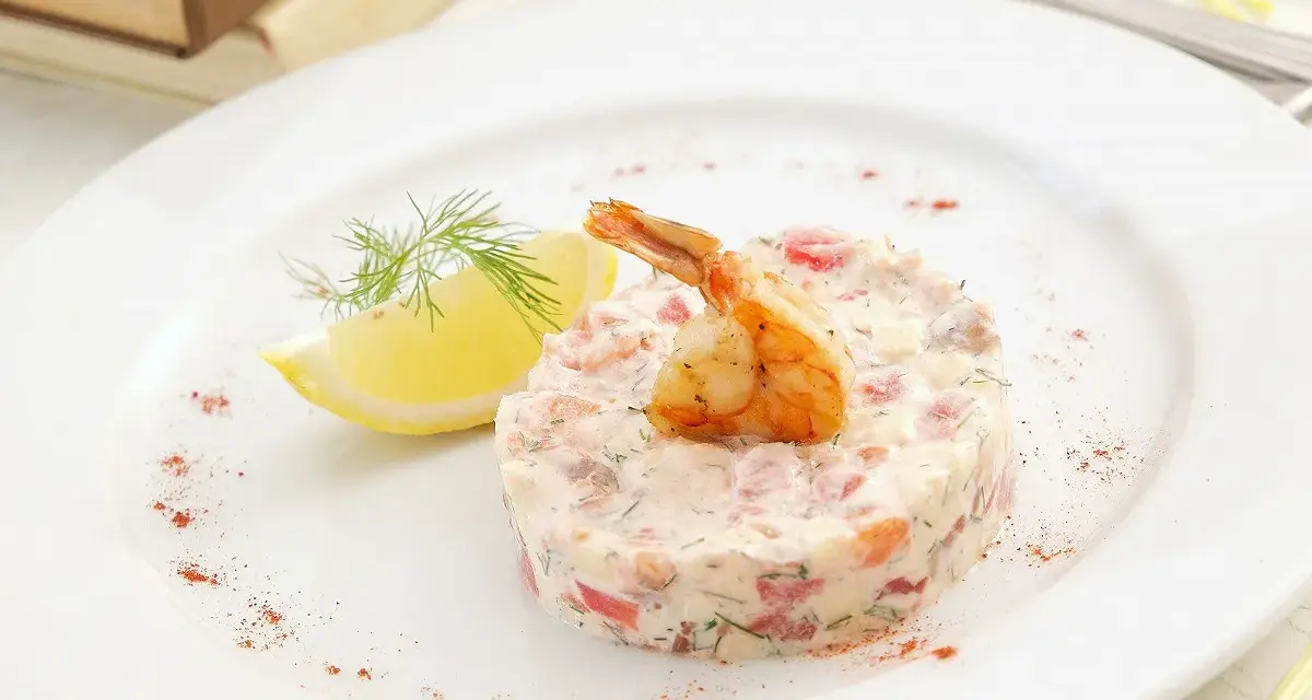 Délicieux tartare de crevette thaï, garni d'une crevette grillée et d'une tranche de citron, sur une assiette blanche.