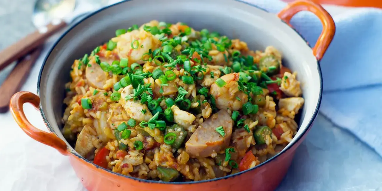 Un plat de jambalaya coloré, garni de crevettes, poulet, saucisse et oignons verts. Une recette savoureuse à découvrir.