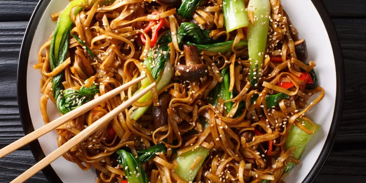 Un plat de chow mein appétissant avec des nouilles, des légumes verts croquants, des champignons et des poivrons rouges, saupoudré de graines de sésame.