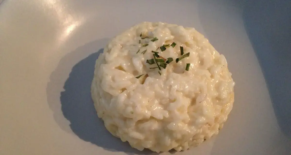 Un crémeux risotto coco, parsemé de ciboulette fraîche, repose sur une assiette claire.