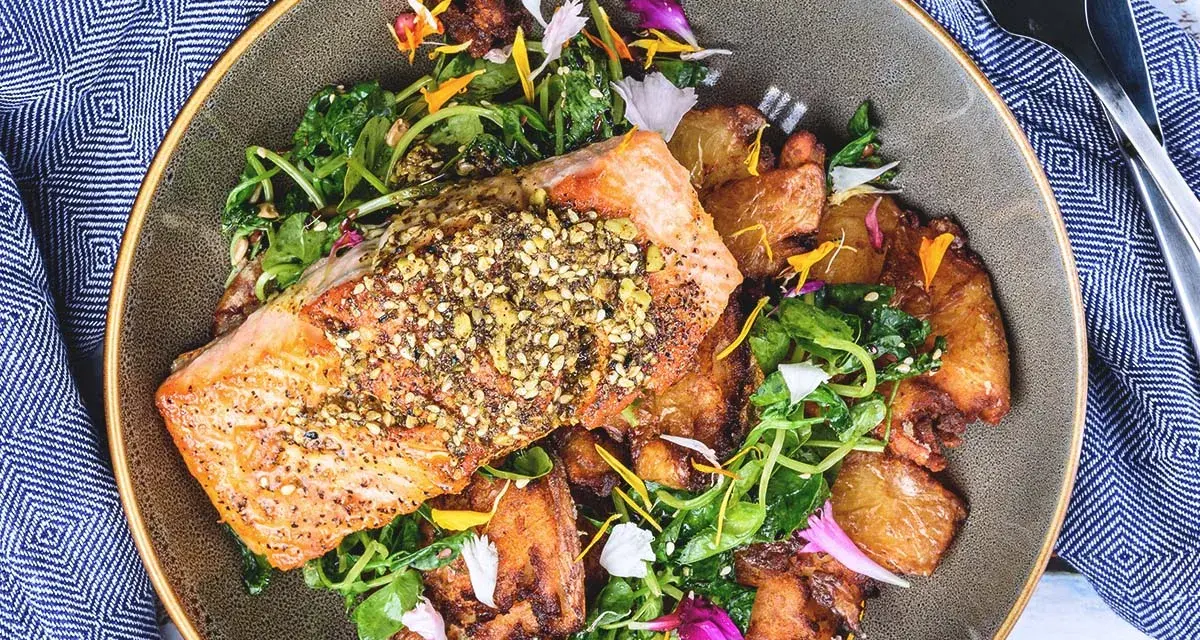 Un filet de saumon croustillant, garni de graines, servi avec des pommes de terre rôties et une salade verte. Un accompagnement poisson savoureux et coloré.