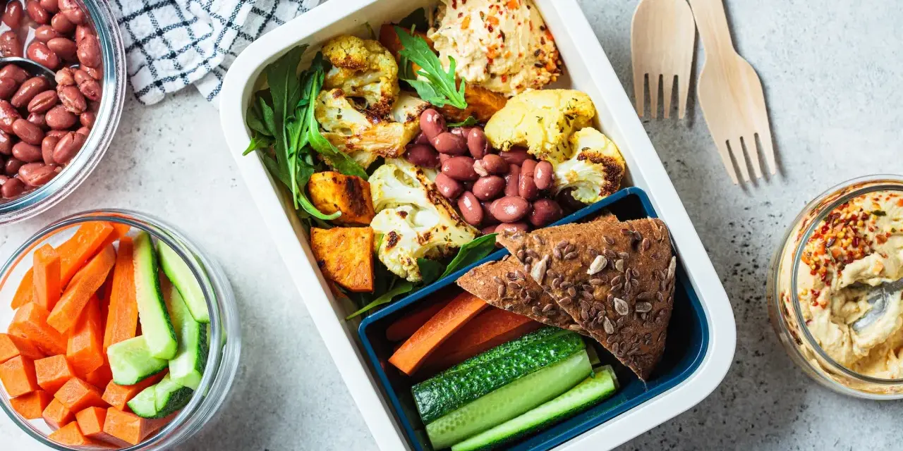 Un repas tiré du sac sain et coloré : houmous, légumes rôtis, haricots rouges, pain complet et crudités. Parfait pour un déjeuner sur le pouce.
