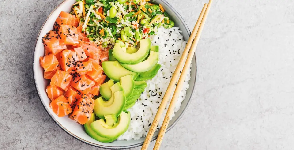 Un délicieux poke bowl santé avec saumon cru, avocat, riz blanc et légumes croquants, prêt à être dégusté avec des baguettes.