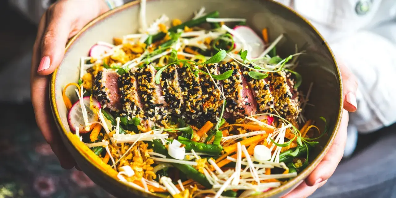 Un délicieux tataki de thon, enrobé de sésame, servi avec un accompagnement coloré de légumes croquants et de pousses fraîches.