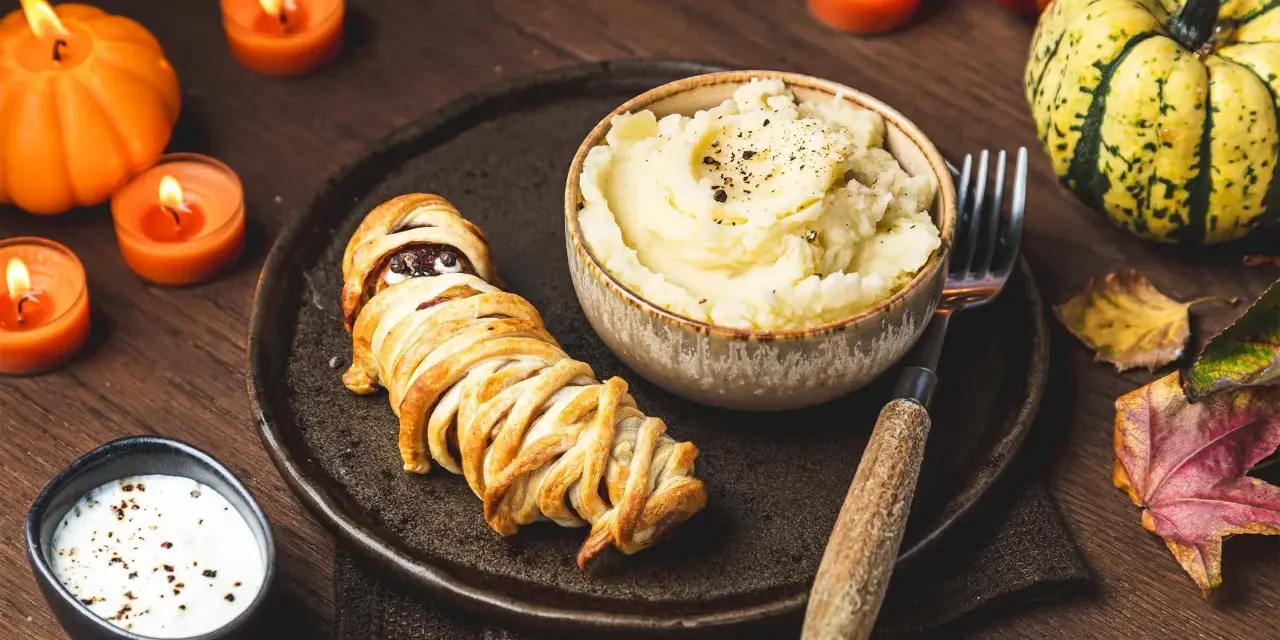 Un délicieux menu d'Halloween pour adultes : une momie feuilletée, purée de pommes de terre et sauce crémeuse, le tout dans une ambiance tamisée par des bougies.