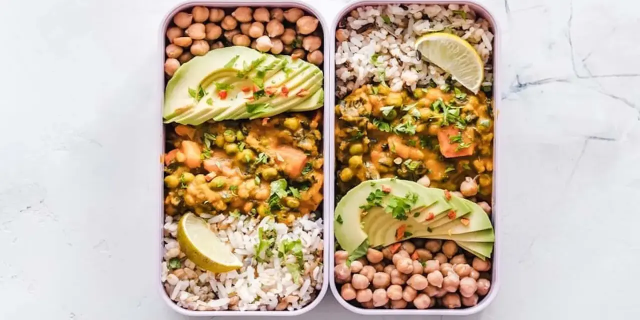 Deux lunch box remplies d'une idée lunch box école saine : curry de légumes, riz, pois chiches et avocat.