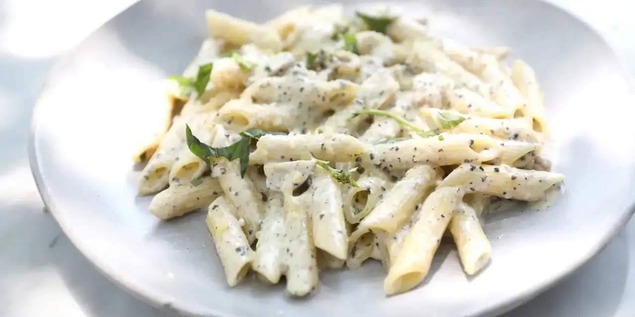 Pâtes penne nappées d'une sauce crémeuse à l'ail, parsemées de fines herbes fraîches, servies sur une assiette blanche.