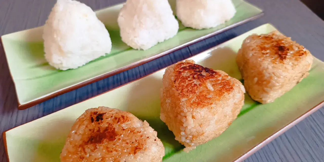 Sur des assiettes vertes, des onigiris nature et grillés, parfaits pour un pique-nique japonais.