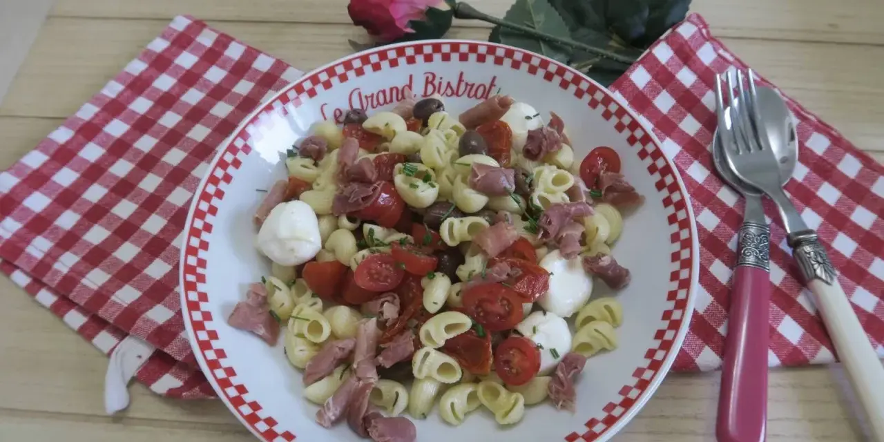 Une savoureuse salade italienne de pâtes avec tomates cerises, mozzarella, olives et jambon cru, garnie de ciboulette.
