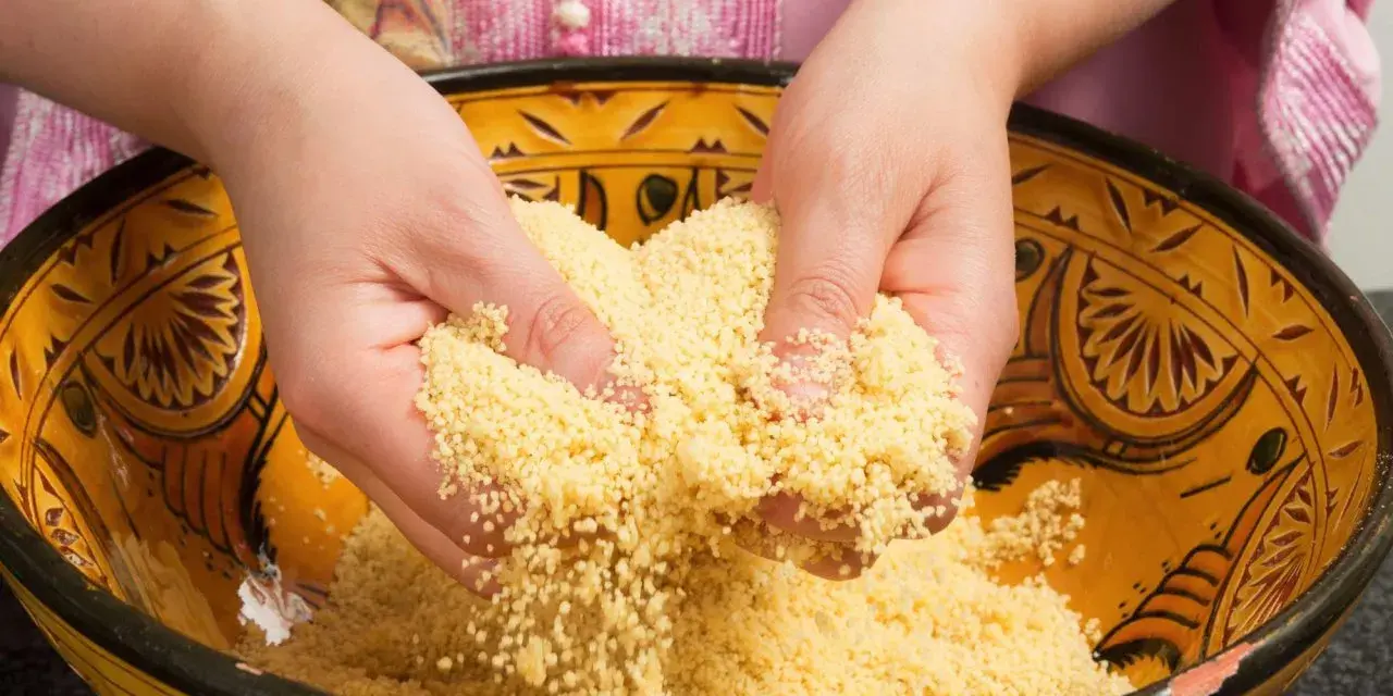 Mains travaillant du couscous marocain dans un plat traditionnel décoré.