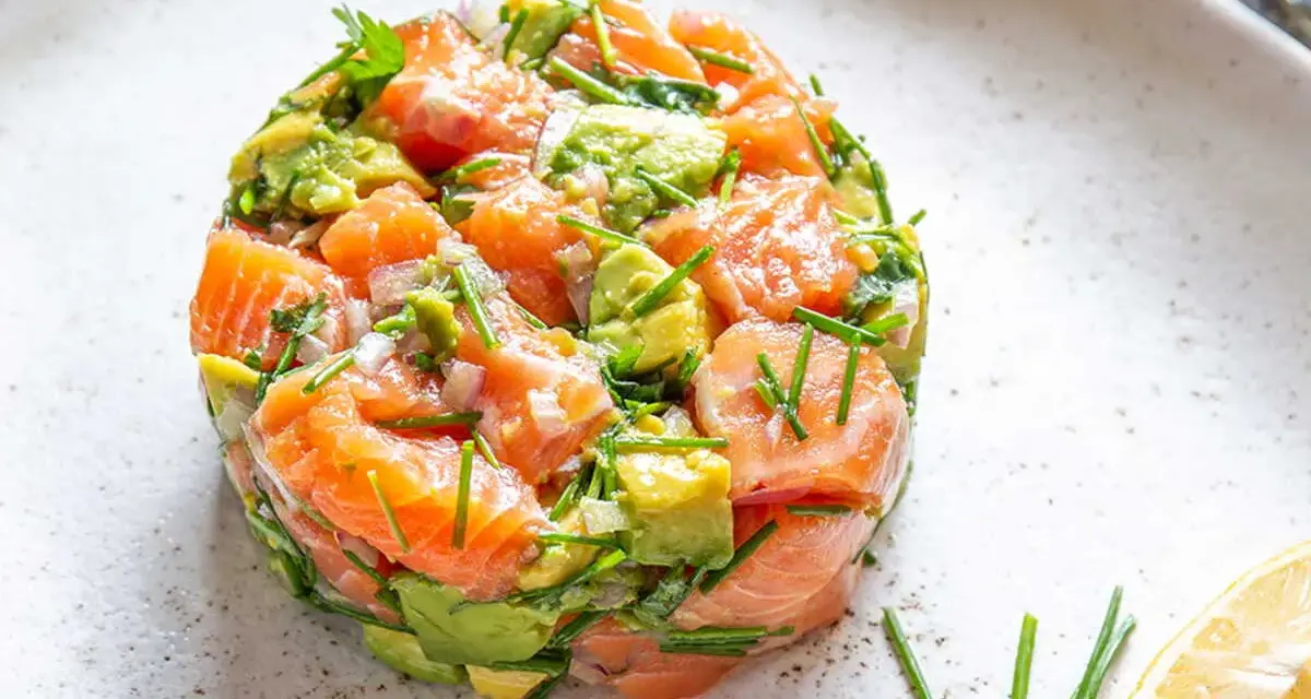 Un délicieux tartare saumon avocat, frais et coloré, garni de ciboulette et servi avec un quartier de citron.