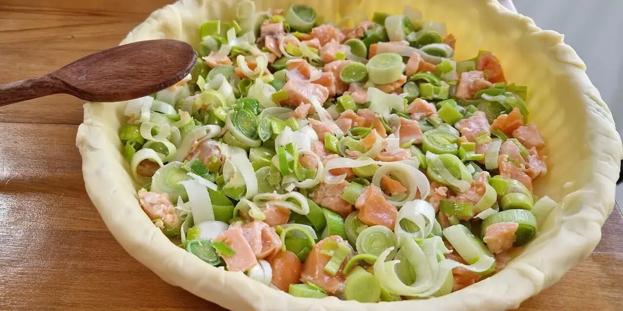 Préparation d'un plat végétarien : une tarte garnie de saumon et de poireaux coupés, prête à être cuite.