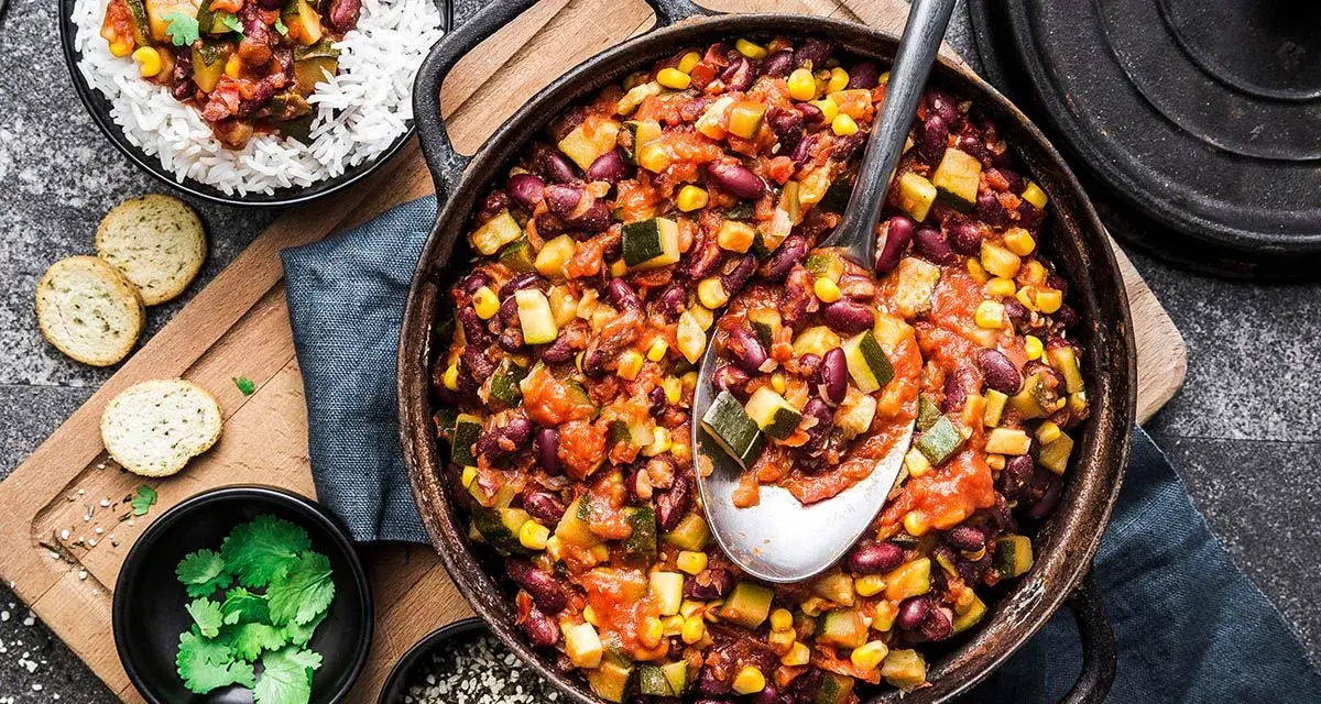 Un plat de chili végétarien copieux avec des haricots rouges, du maïs et des courgettes, servi avec du riz blanc.