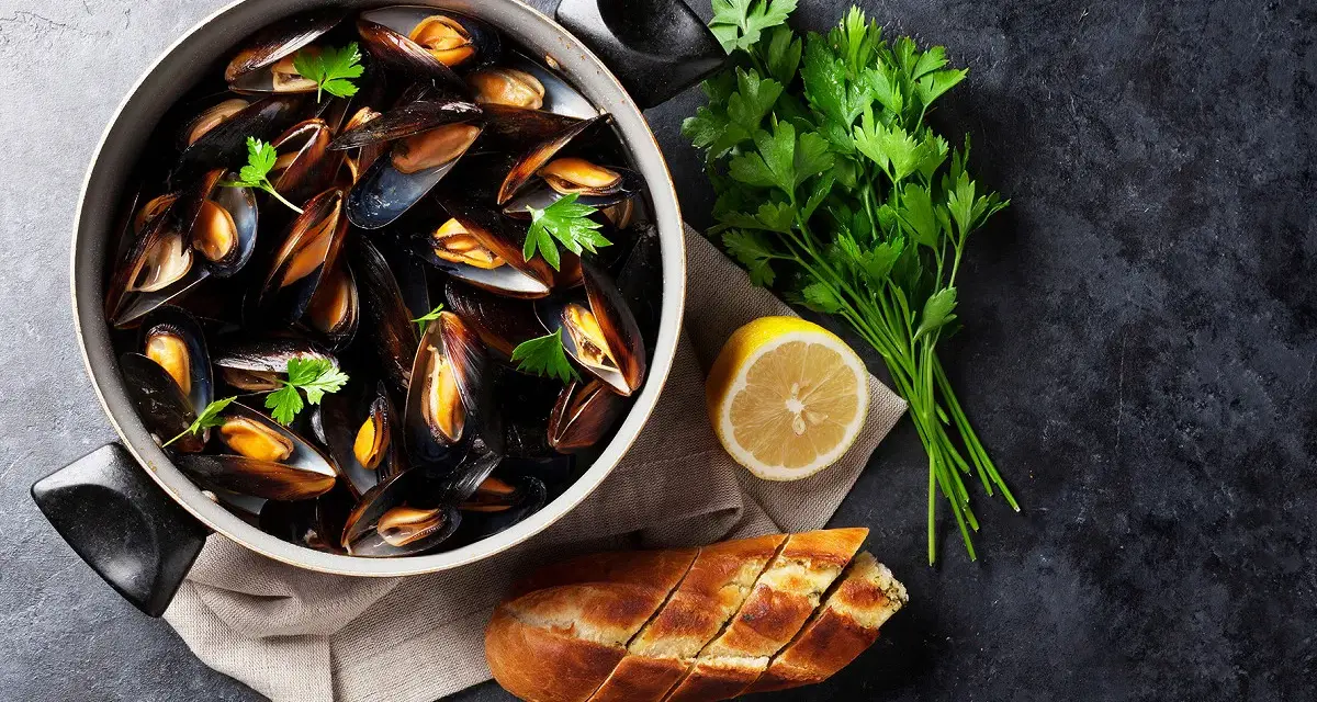Un plat de moules au rosé, garni de persil frais, avec un quartier de citron et une baguette à l'ail.