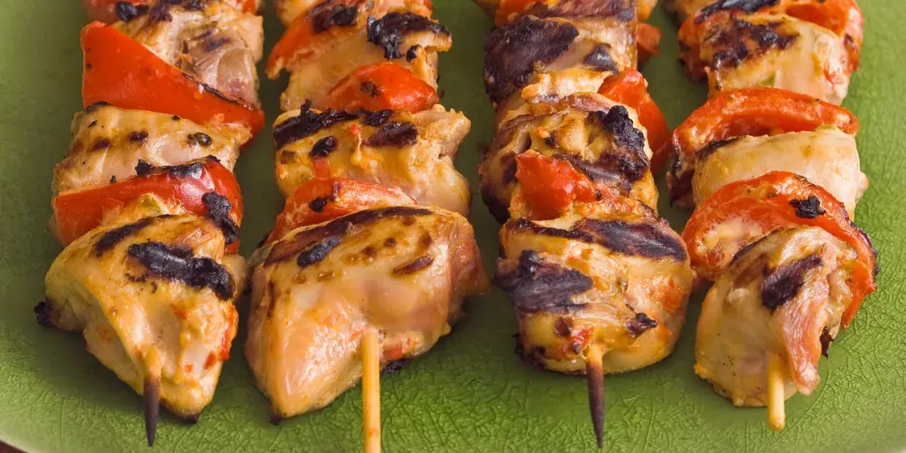 Brochettes de poulet grillé avec poivrons rouges sur une assiette verte. Parfait pour savoir quoi servir avec des brochettes de poulet.