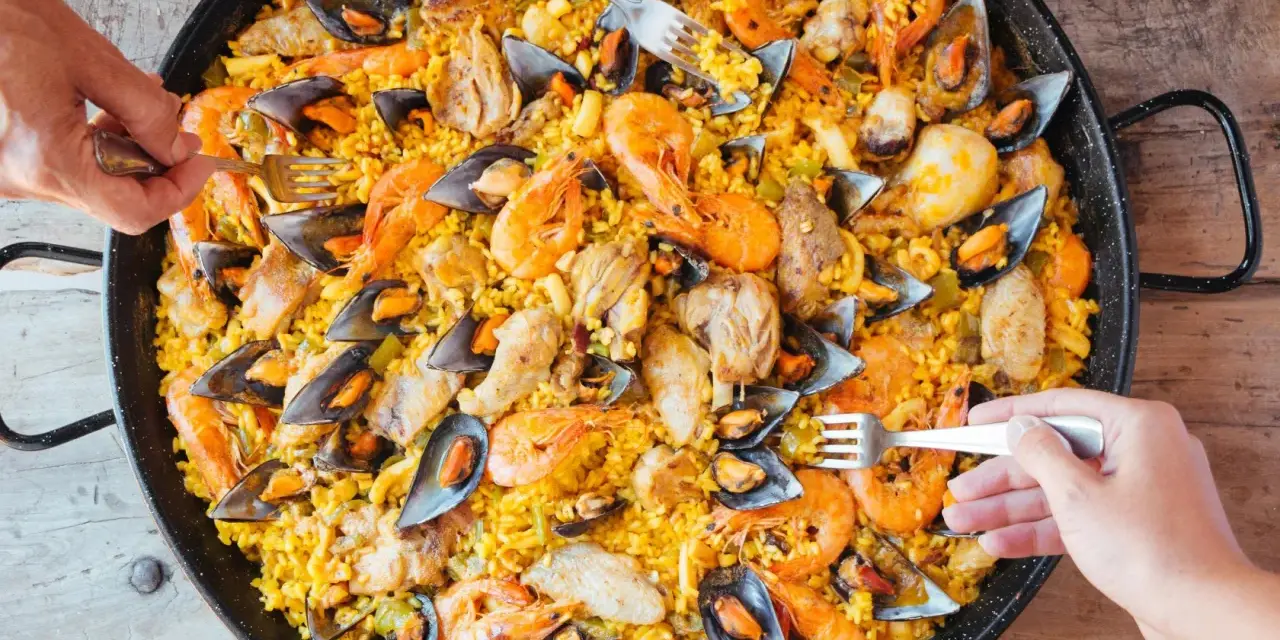 Un plat généreux de poulet paella, garni de crevettes et de moules, prêt à être dégusté par plusieurs mains.
