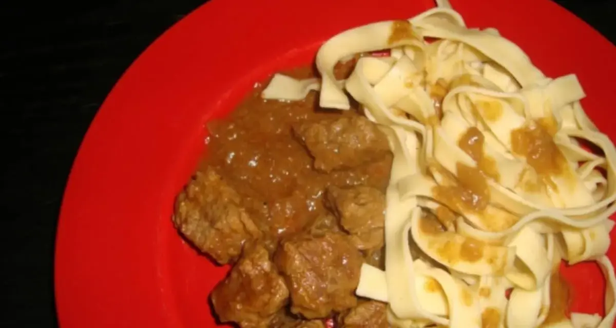 Un plat de pâtes fraîches avec un riche boeuf vindaloo, servi sur une assiette rouge vif.