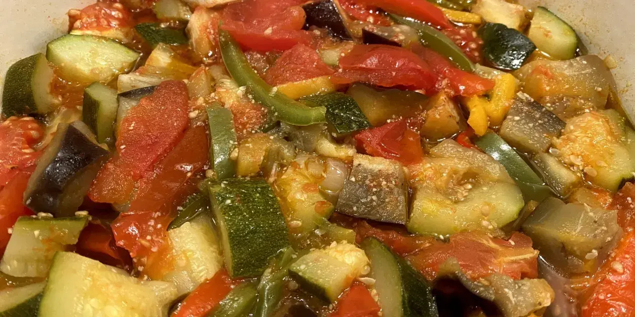 Un plat coloré de ratatouille niçoise, avec des morceaux de courgettes, aubergines, tomates et poivrons mijotés.