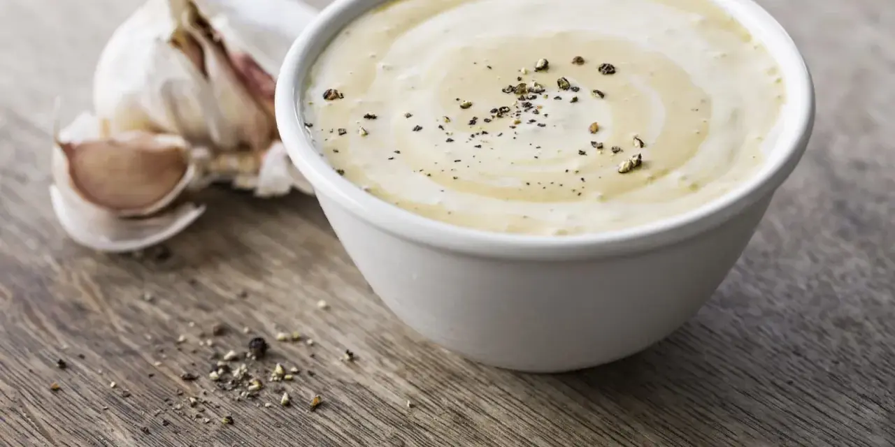 Sauce césar sans oeuf crémeuse, parsemée de poivre noir, avec une tête d'ail en arrière-plan sur fond de bois.