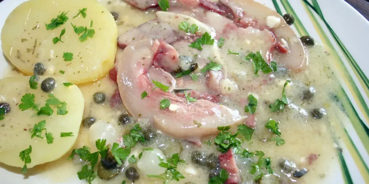 Tête de veau en sauce avec des pommes de terre et des câpres, garnie de persil frais.