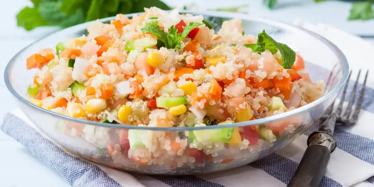 Salade quinoa colorée avec des dés de tomates, carottes, concombre et maïs, garnie de feuilles de menthe fraîche.