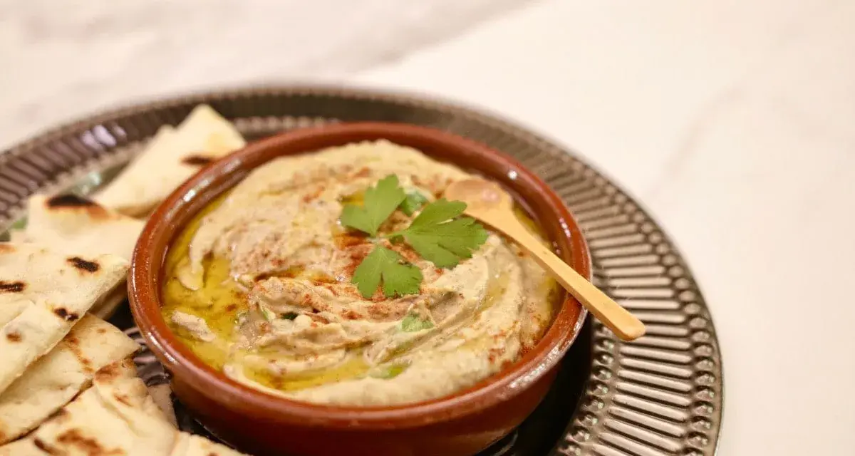 Un bol de baba ganoush crémeux, garni de persil frais et d'un filet d'huile d'olive, servi avec des pains pita grillés.