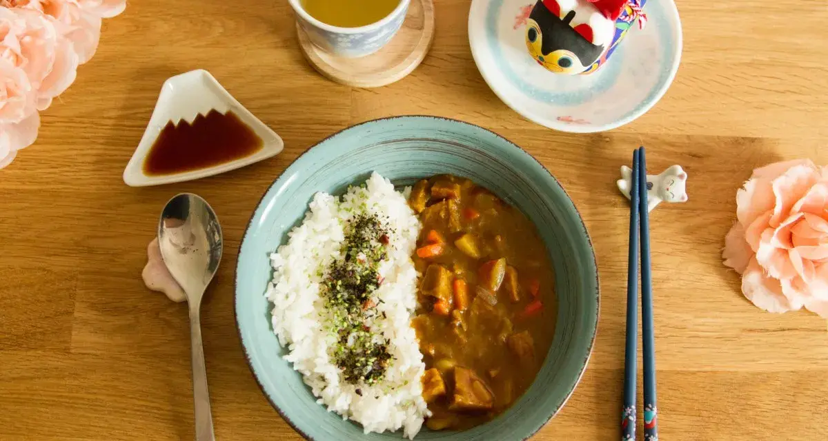 Un délicieux curry japonais avec du riz blanc, servi avec une tasse de thé et des décorations mignonnes.