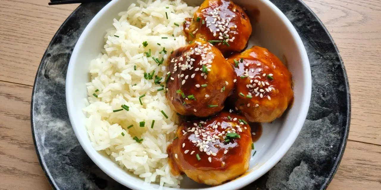 Délicieuses boulettes de poulet asiatique nappées d'une sauce sucrée et salée, servies avec du riz blanc et parsemées de graines de sésame.