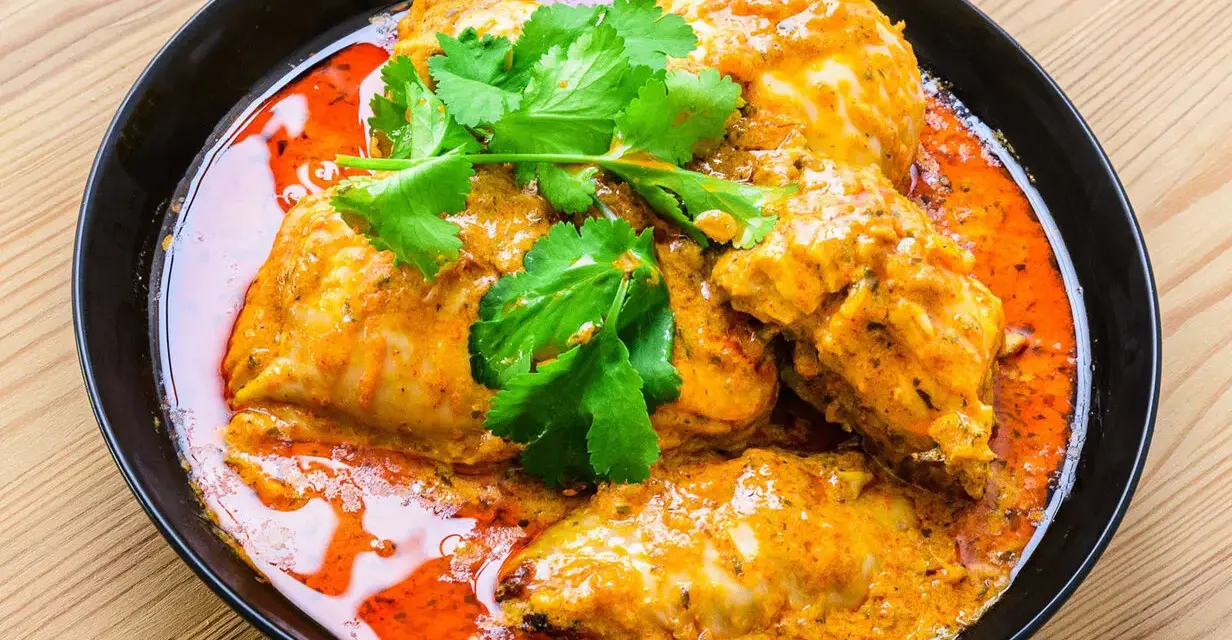 Un plat de poulet vindaloo, un curry indien épicé, servi dans un bol noir avec de la coriandre fraîche.