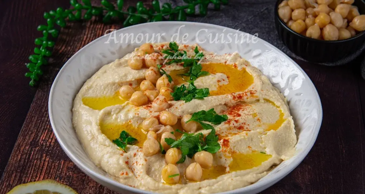 Un plat de houmous crémeux, garni de pois chiches, persil et paprika. Parfait pour découvrir 7 recettes de houmous maison.
