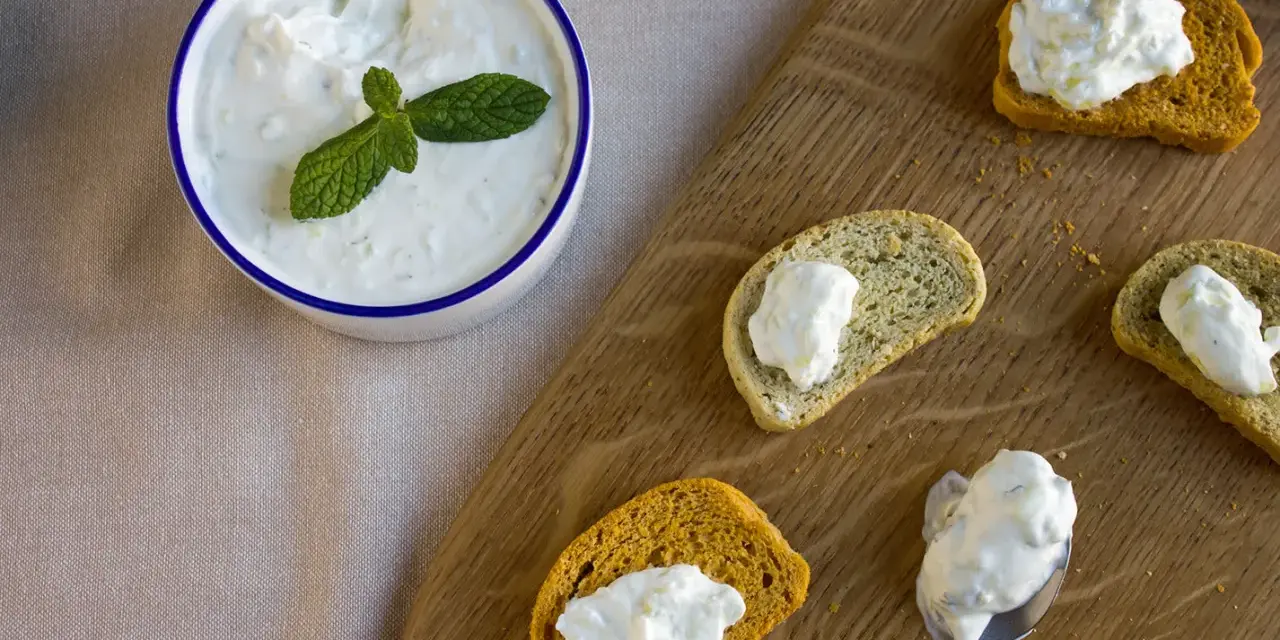 Un bol de crème tzatziki frais, garni de menthe, est servi avec des toasts.