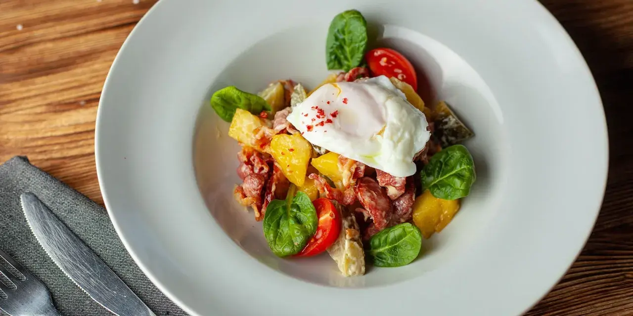 Salade colorée avec œuf poché, tomates cerises, lardons et quelques feuilles de salade légumes verts.